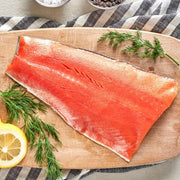 Raw salmon fillet on a wooden board with lemon slices and herbs, placed on a striped cloth.