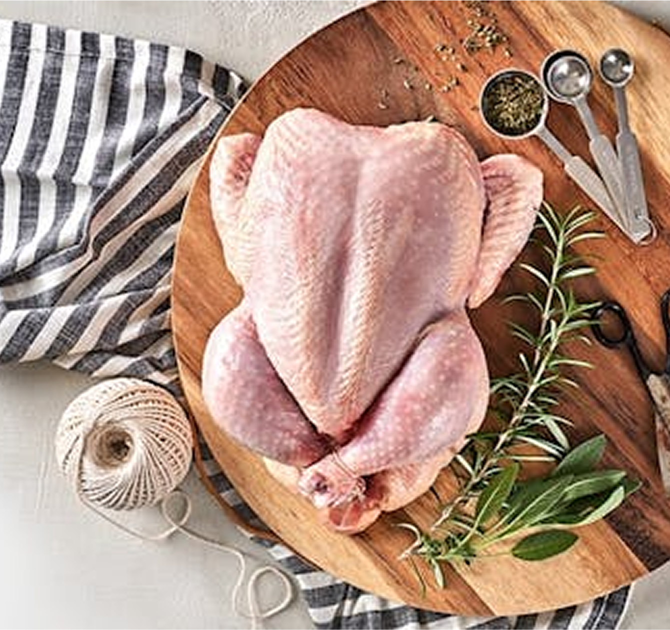 Raw chicken on a wooden cutting board with herbs and measuring spoons