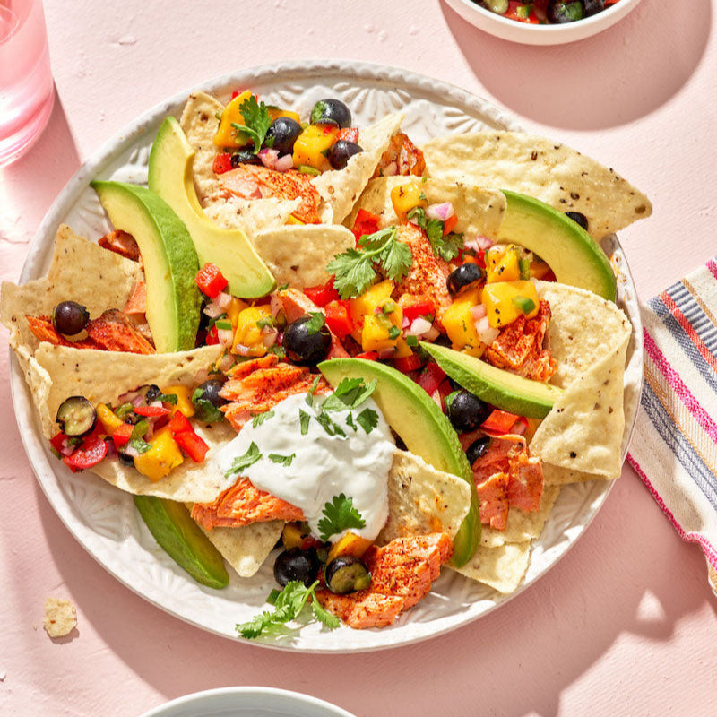 Plate of colorful nachos with toppings on a pink surface