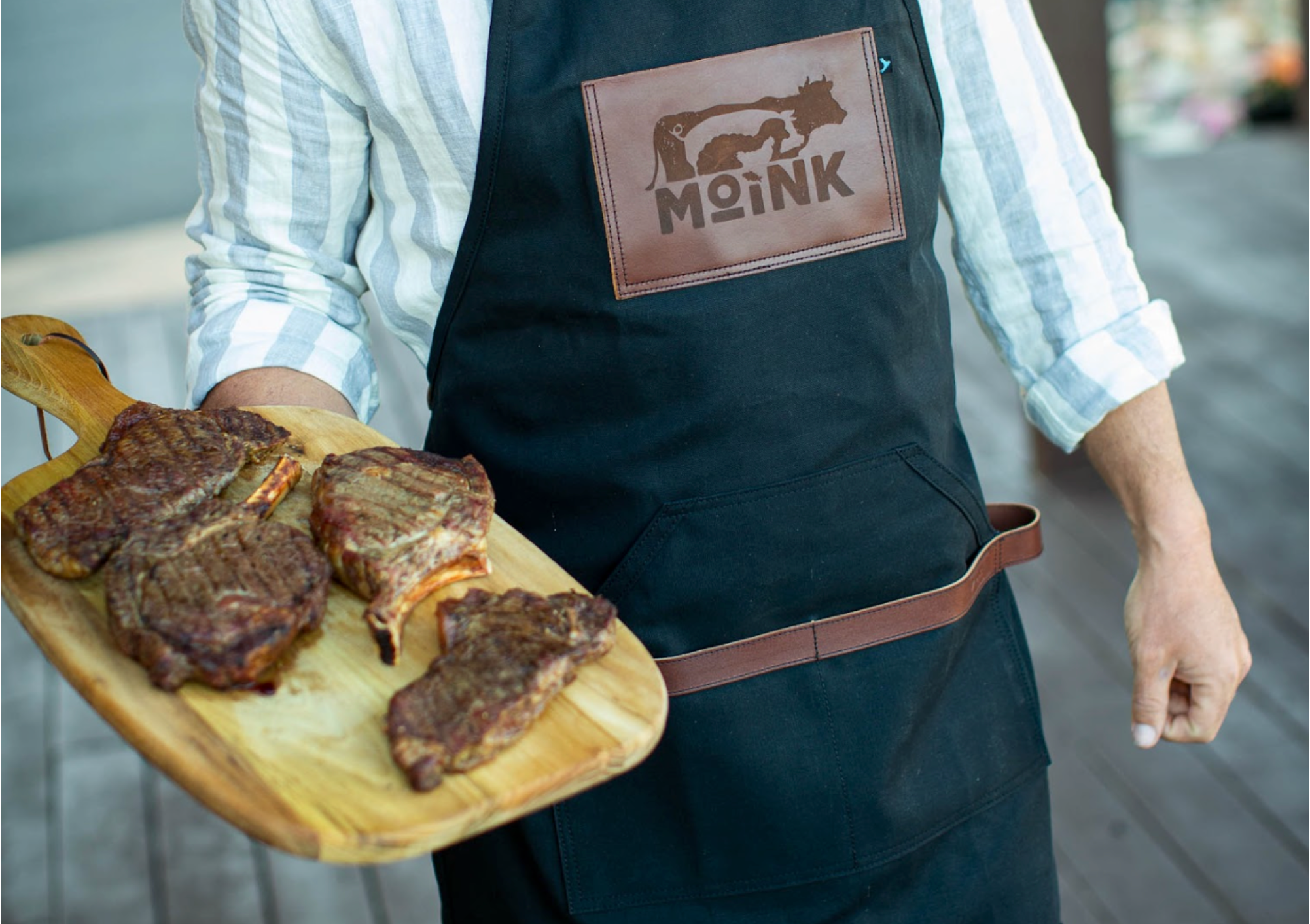 Person wearing a black apron with 'Moink' branding, holding a tray of food.