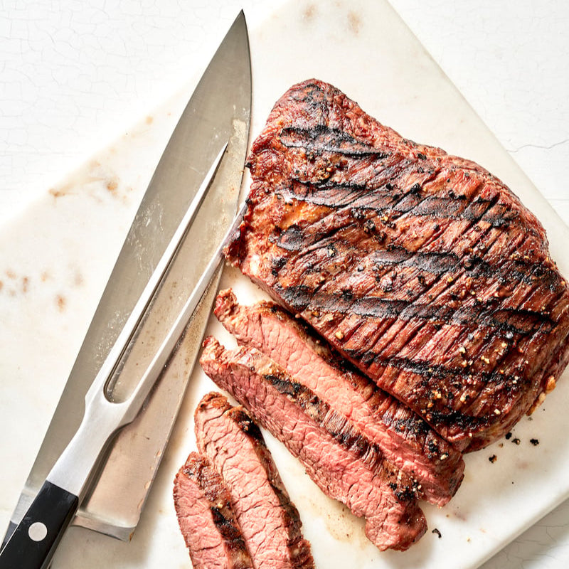 Grilled steak with slices cut on a marble board with a knife.