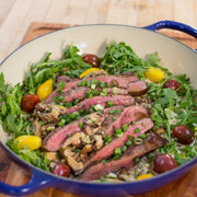 Steak salad with arugula, grapes, and lemon in a blue skillet on a wooden cutting board.