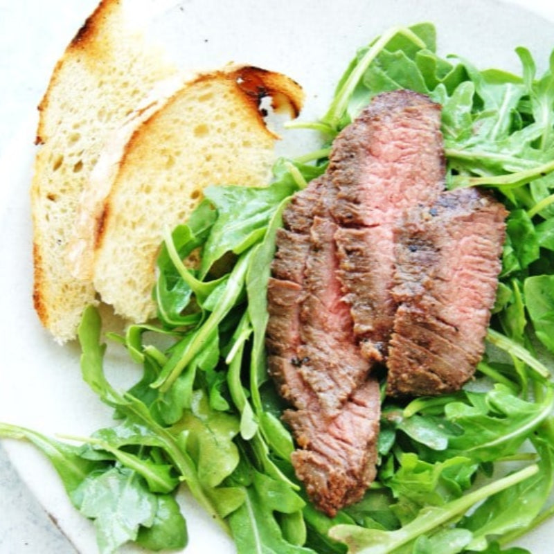 Grilled steak on arugula with toasted bread on a white plate.