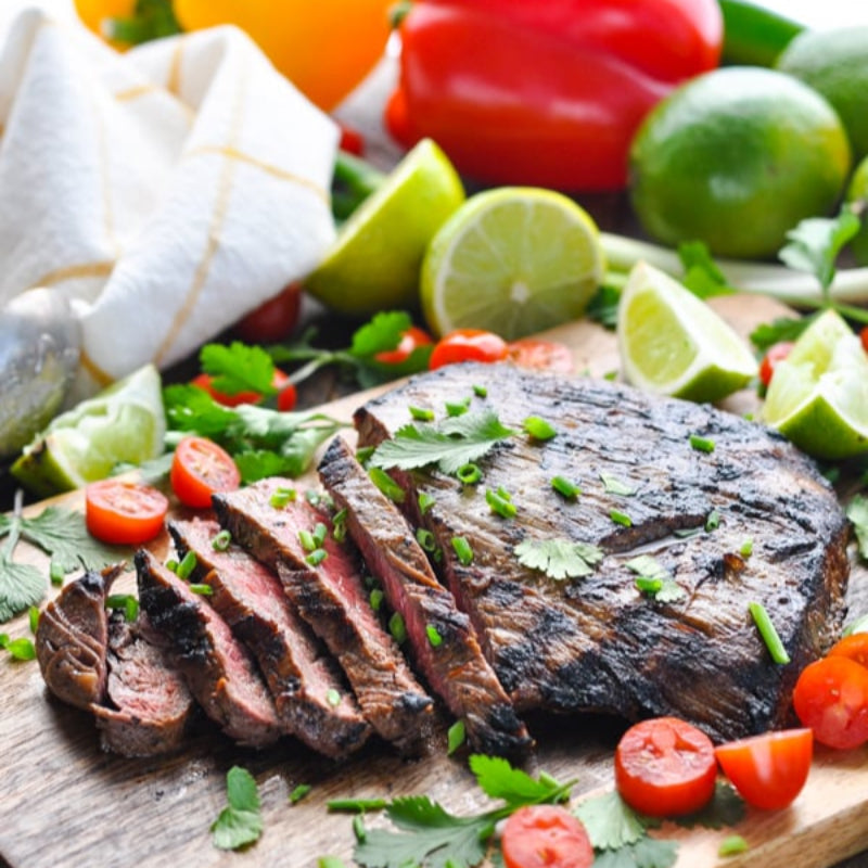Grilled steak on a wooden cutting board with vegetables and herbs.
