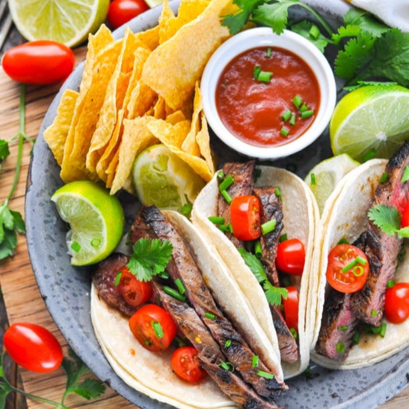 Steak tacos with tortilla chips and salsa on a wooden board.