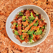 Bowl of beef and broccoli over rice on a cork surface