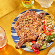 Grilled steak with vegetables on a striped plate on a yellow tablecloth.