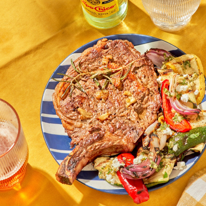 Grilled steak with vegetables on a striped plate on a yellow tablecloth.
