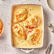 Baked chicken with creamy sauce in a white dish on a speckled countertop.