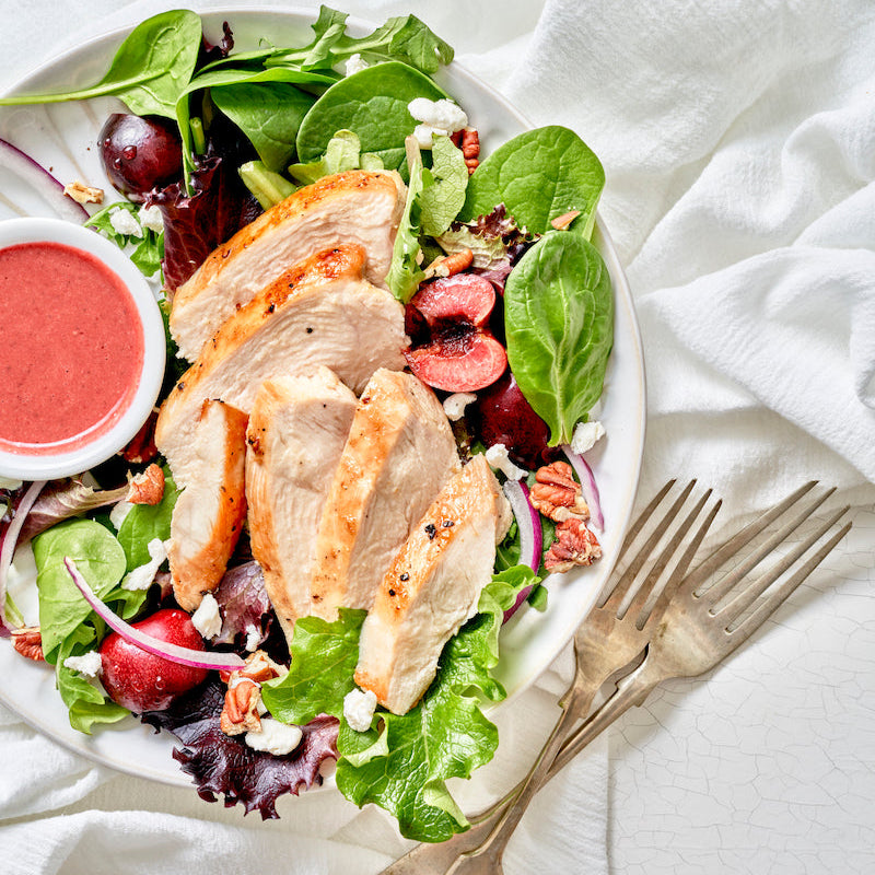Salad with chicken, grapes, and walnuts on a white plate with a fork and dressing on a white cloth.