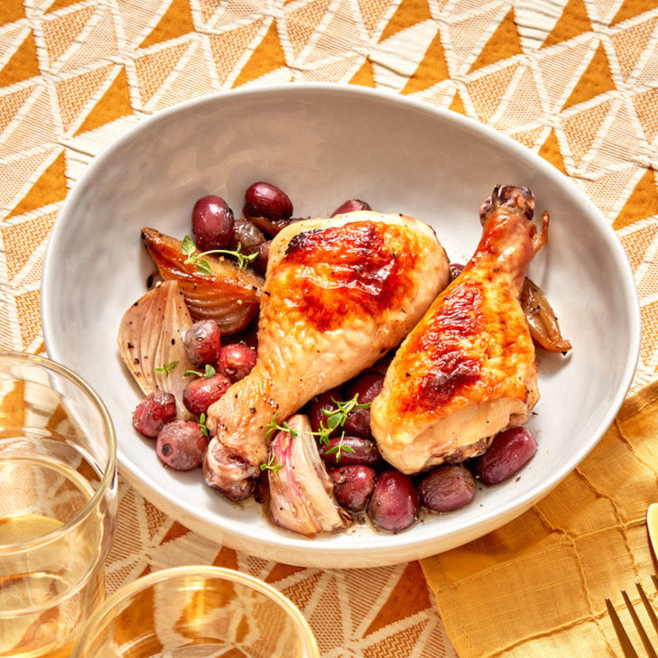 Bowl of roasted chicken with grapes on a patterned tablecloth