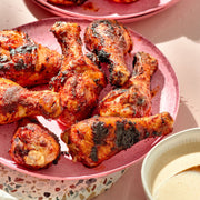 Spicy chicken drumsticks on a pink plate with a side of dipping sauce.