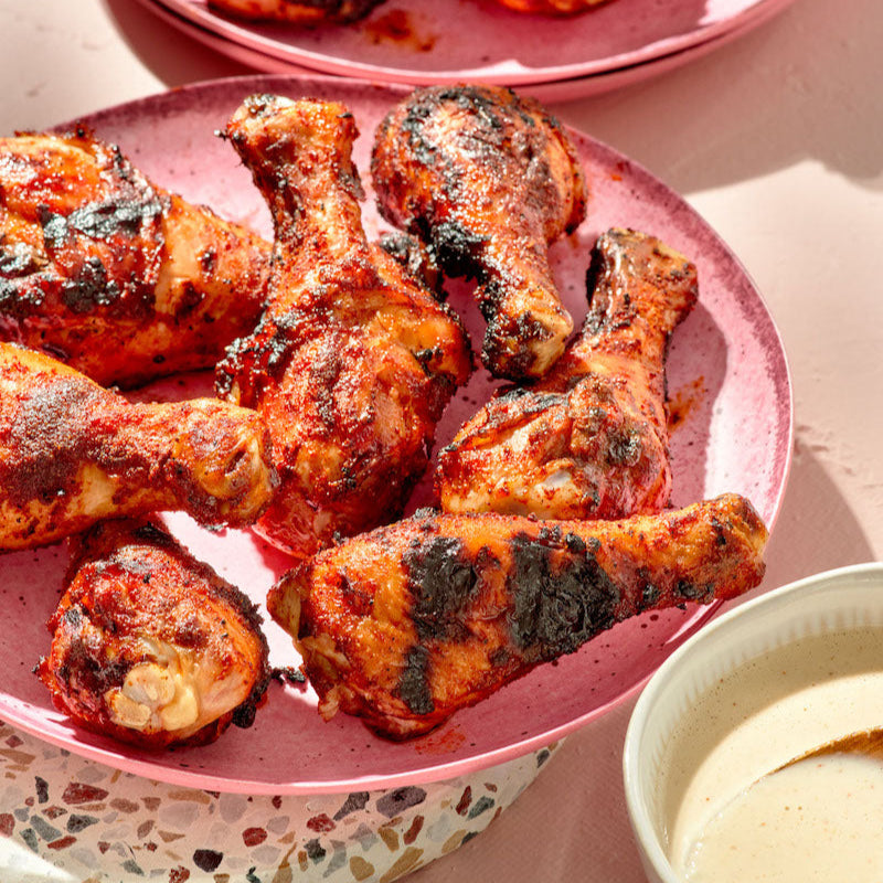 Spicy chicken drumsticks on a pink plate with a side of dipping sauce.
