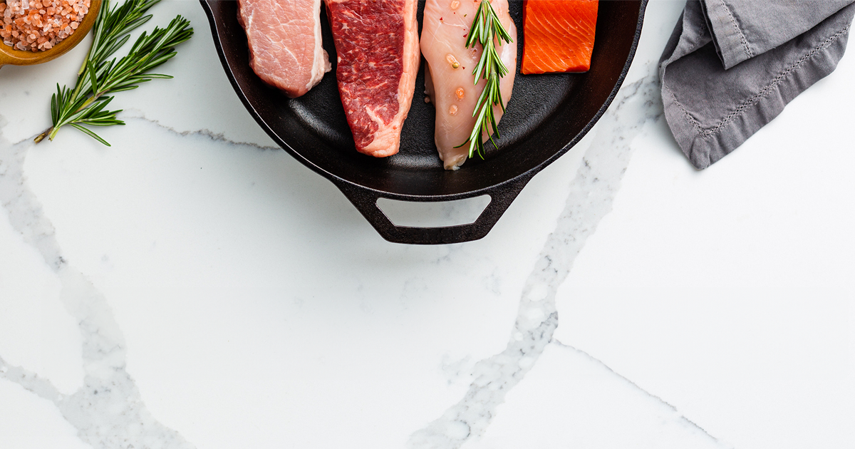 Raw meats on a black plate with rosemary on a marble surface
