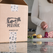 Box with Moink branding on a kitchen counter with a person preparing food.
