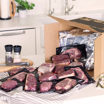 Box of MOINK meat packages on a kitchen counter with packaging materials.