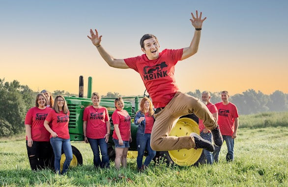 Person in red shirt jumping in a field with others around, under a clear sky.