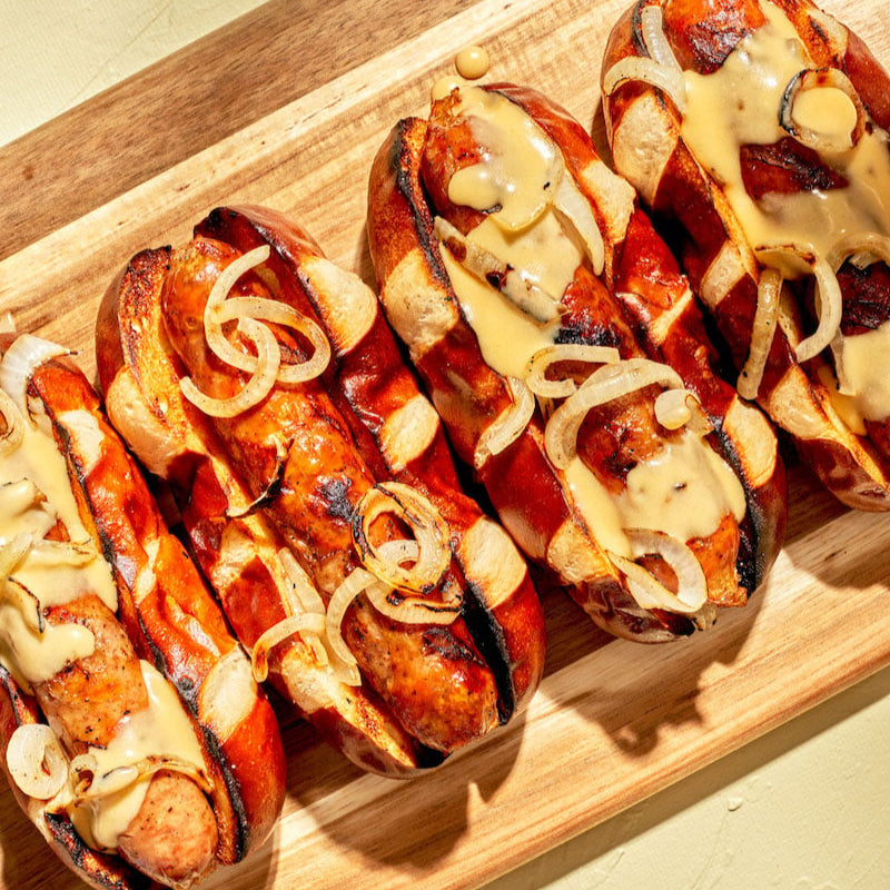 Hot dogs with mustard and onions on a wooden board.