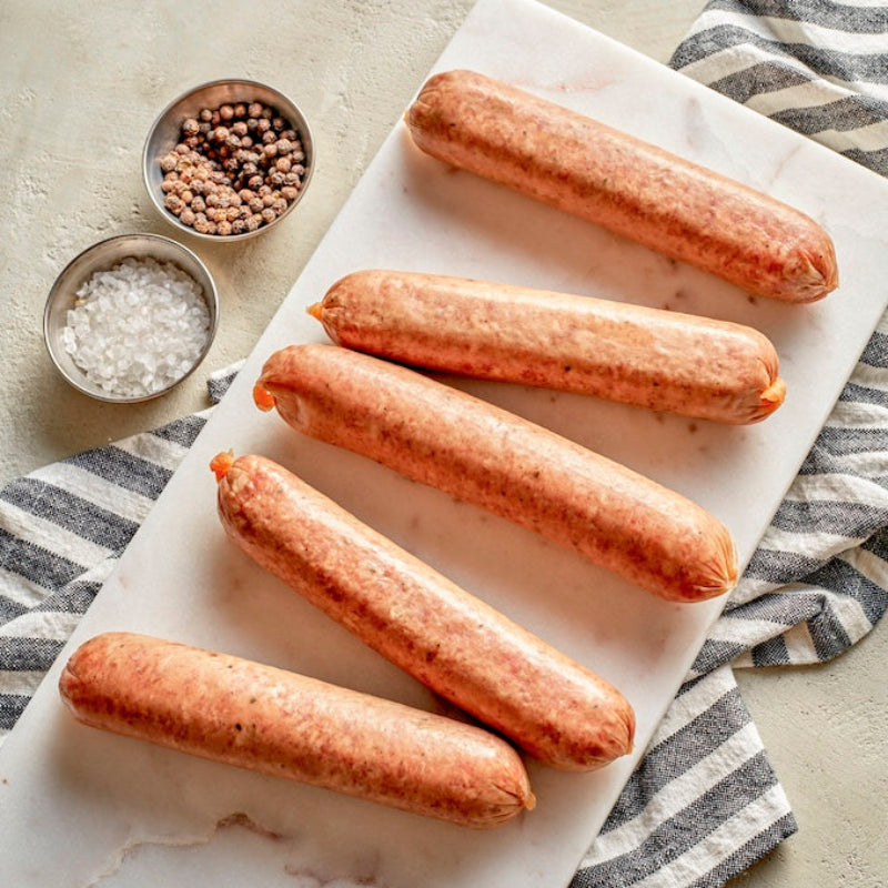 A set of raw bacon brats on a white surface, with salt and spices in the background.
