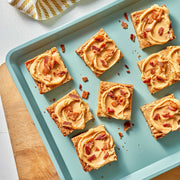 Square cookie bars with peanut butter frosting and bacon bits on a baking tray.