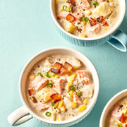 Two bowls of chicken corn chowder with bacon and green onions on a blue background.
