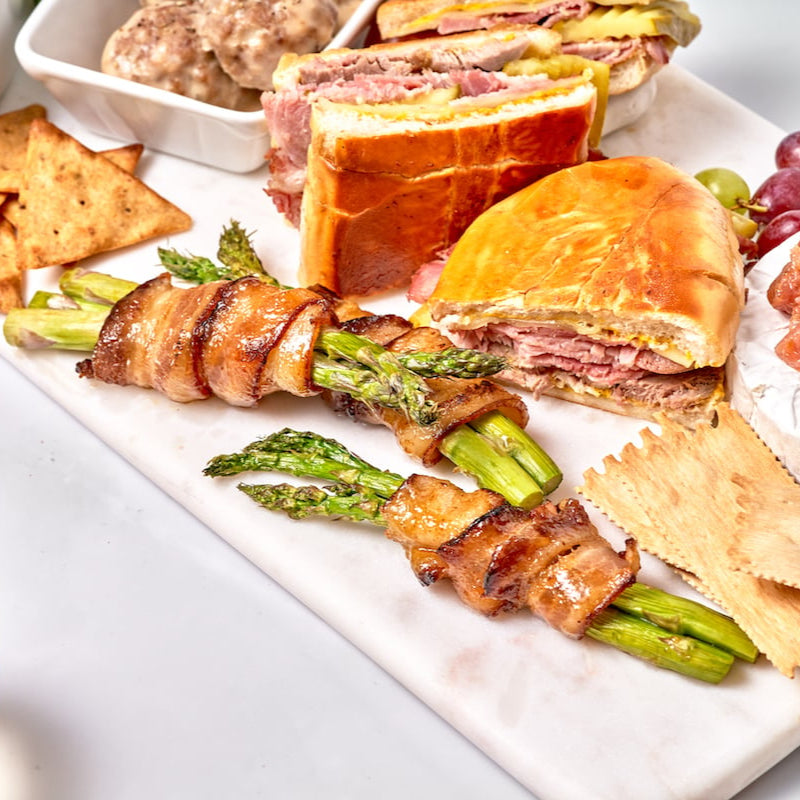 Platter of food including sandwiches and asparagus with a glass of wine.