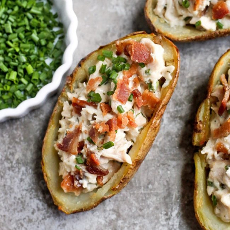 Potato skins filled with chicken salad and bacon on a gray surface.