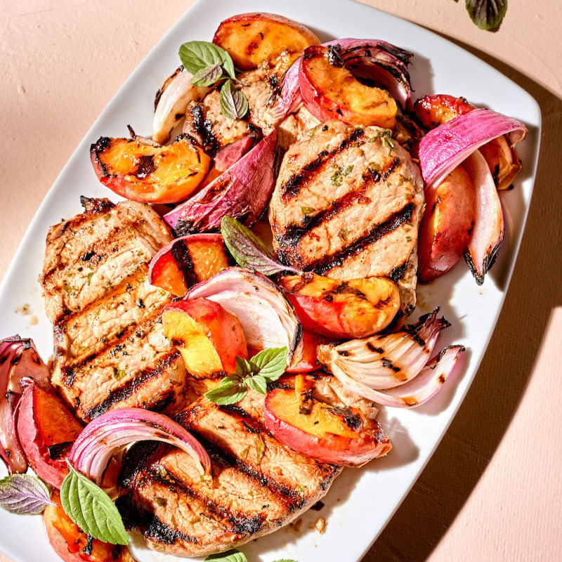 Grilled pork chops with peaches and onions on a white plate.