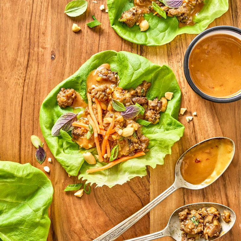 Lettuce wraps with ground meat and vegetables on a wooden surface.