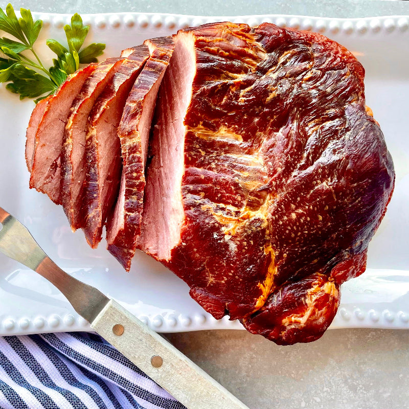 Sliced ham on a white plate with a carving knife and fork.