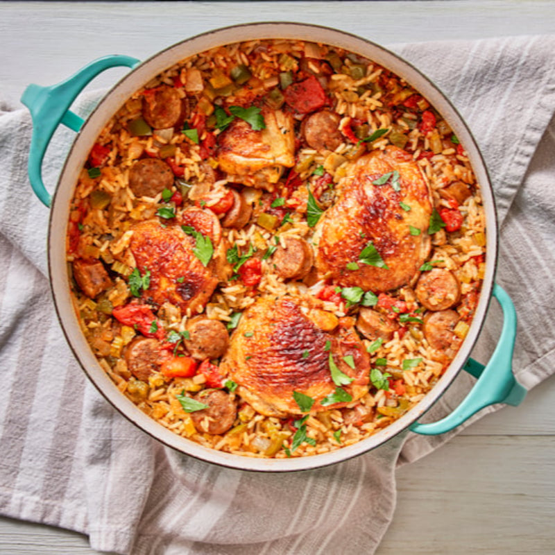 Pot of paella with chicken and sausage on a wooden table.