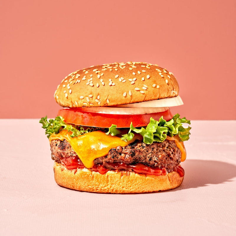 Hamburger with cheese, lettuce, and tomato on a pink background