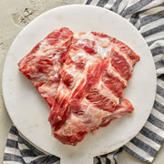 Raw pork ribs on a white plate with a striped napkin to the side.