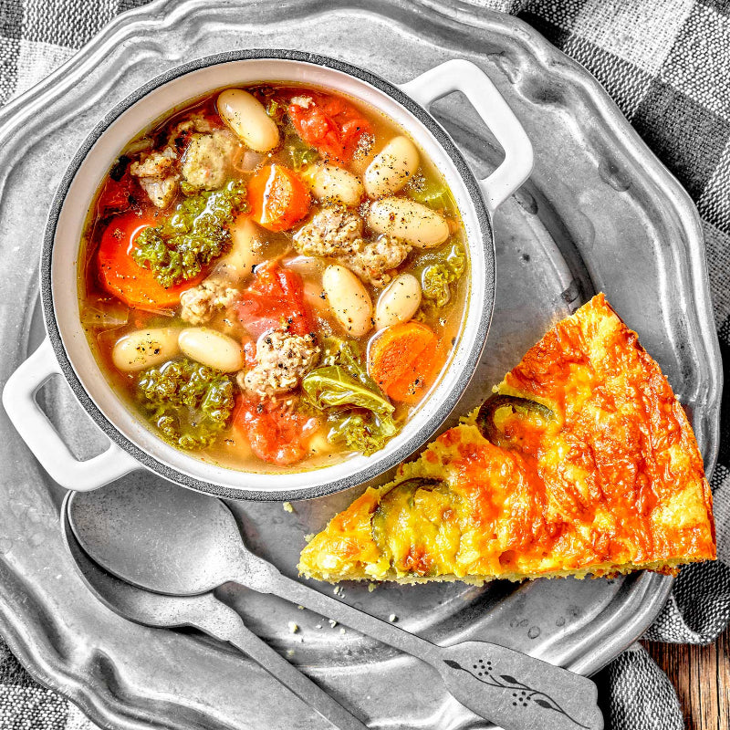 Bowl of soup with vegetables and a slice of pizza on a metal tray.