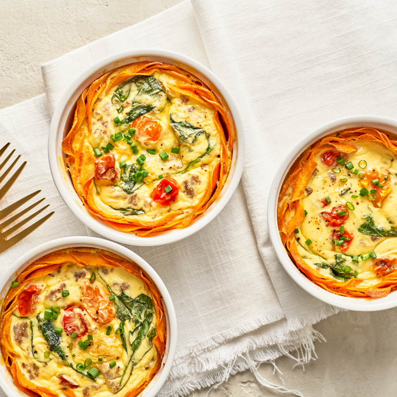 Three small quiches in white bowls on a textured cloth with gold forks.