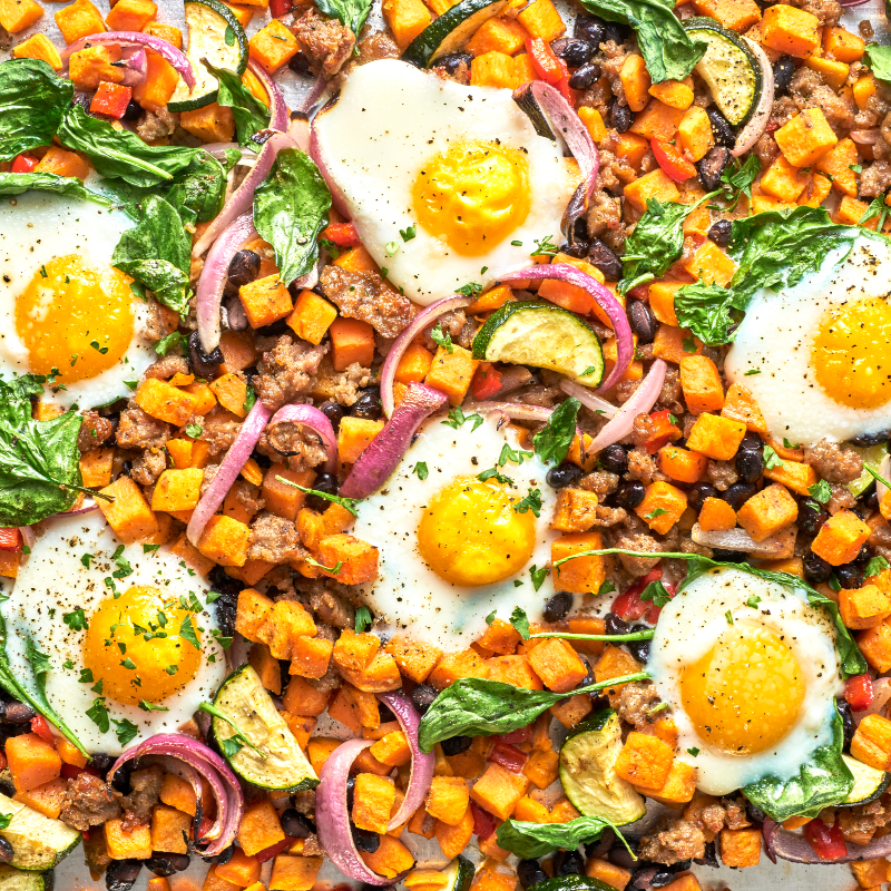 Sheet pan with sweet potato hash, eggs, and vegetables.