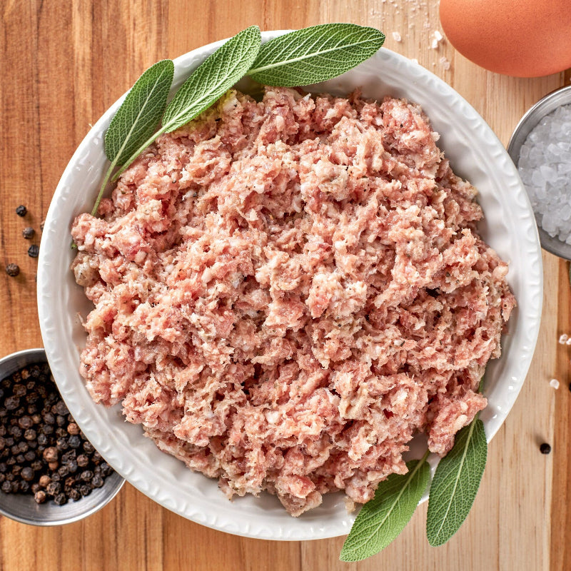 A bowl of ground pork breakfast sausage meat, with sage leaves and spices visible.