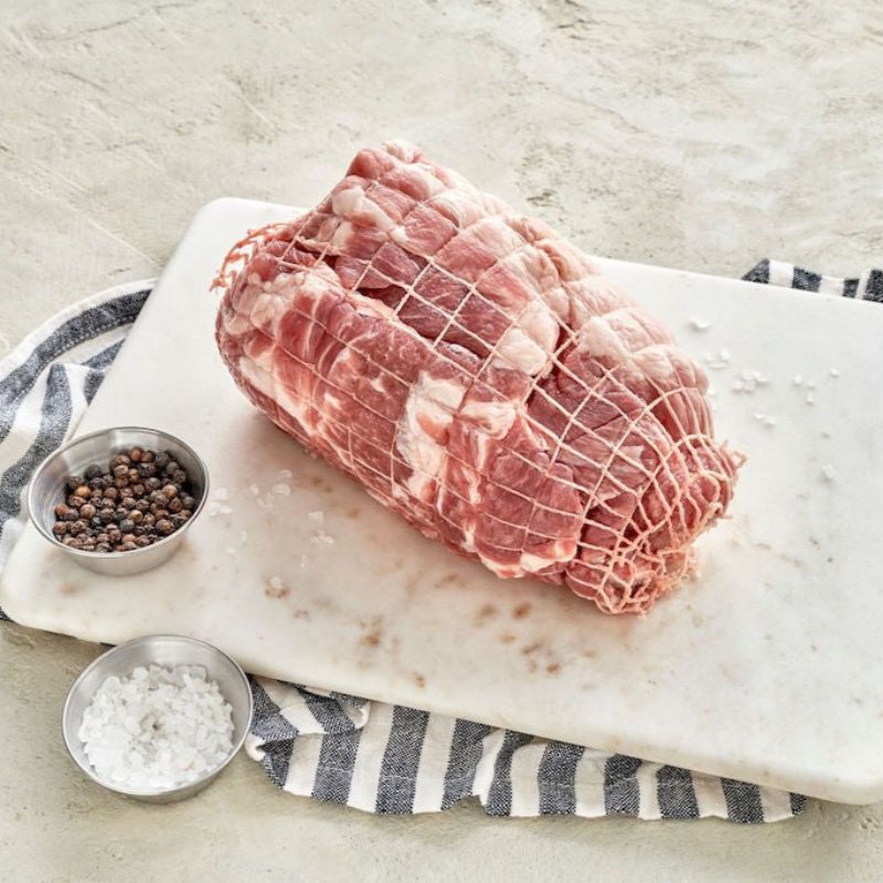 Raw pork roast on a cutting board with salt, pepper, and a towel.