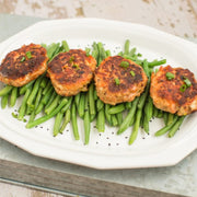 Four salmon patties on green beans on a white plate.