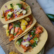 Three salmon tacos with pineapple and onions on a wooden board.