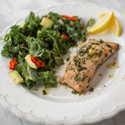 Salmon fillet with kale salad and lemon on a white plate.