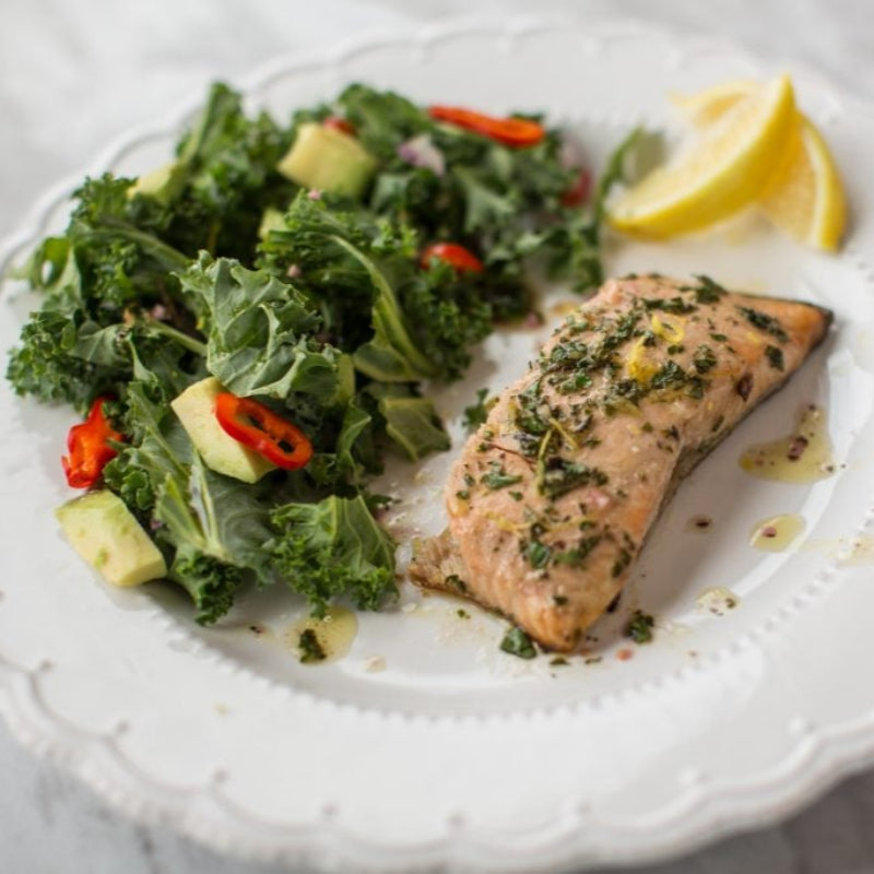 Salmon fillet with kale salad and lemon on a white plate.
