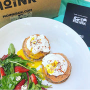 Two baked salmon patties with cream and herbs on a plate with salad, in front of a MoinkBox container.