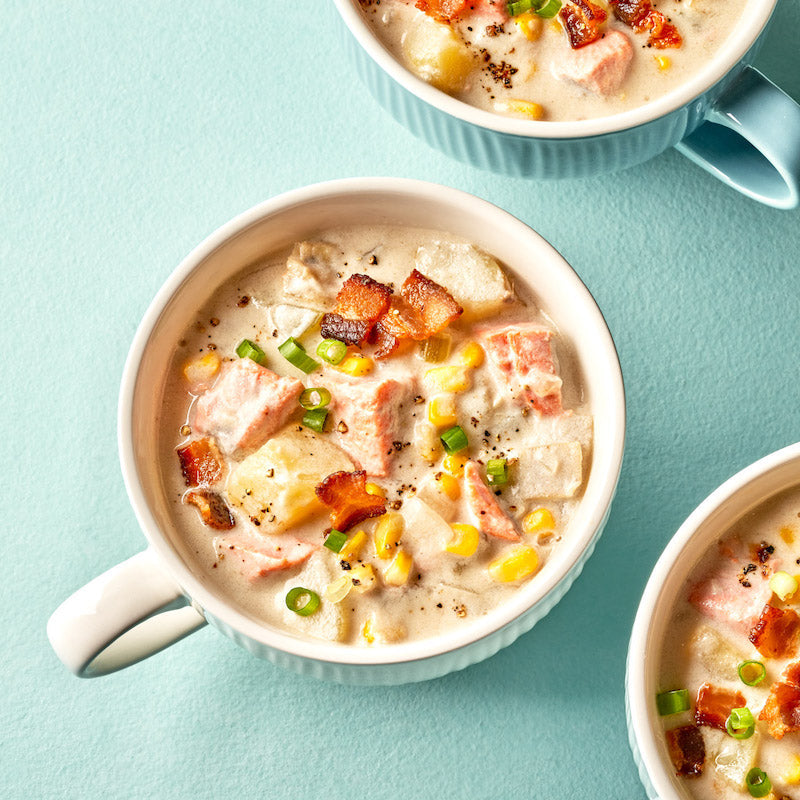 Fish chowder with bacon and corn in a white mug on a blue background.