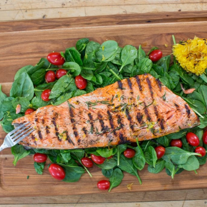 Grilled salmon fillet on a bed of greens and tomatoes on a wooden cutting board.