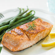 Salmon fillet with green beans and lemon slices on a plate.