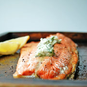 Salmon fillet with herbed butter on a baking tray.