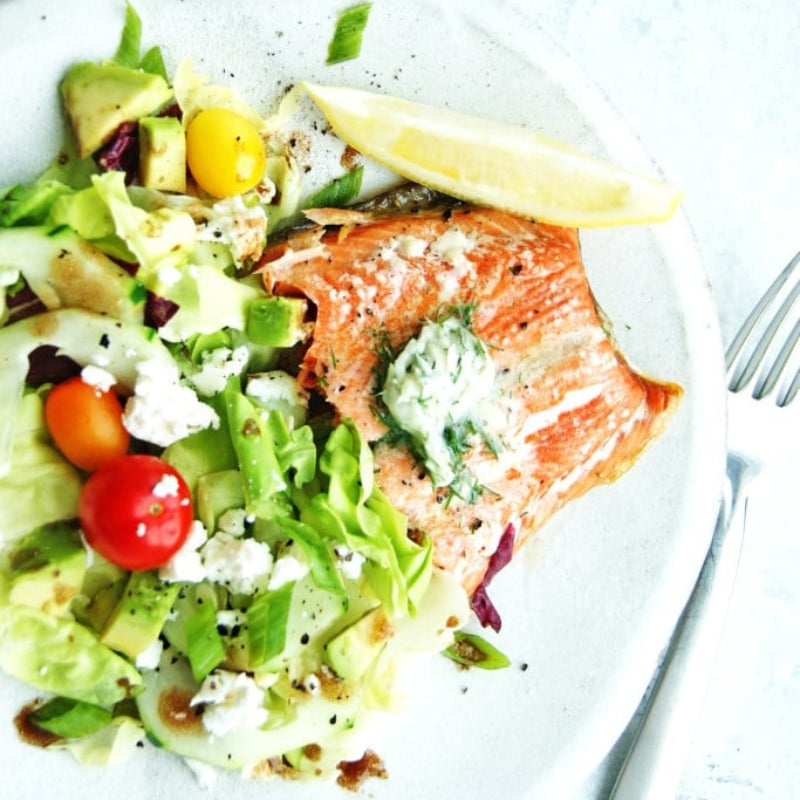 Salmon dish with salad and lemon wedge on a plate.