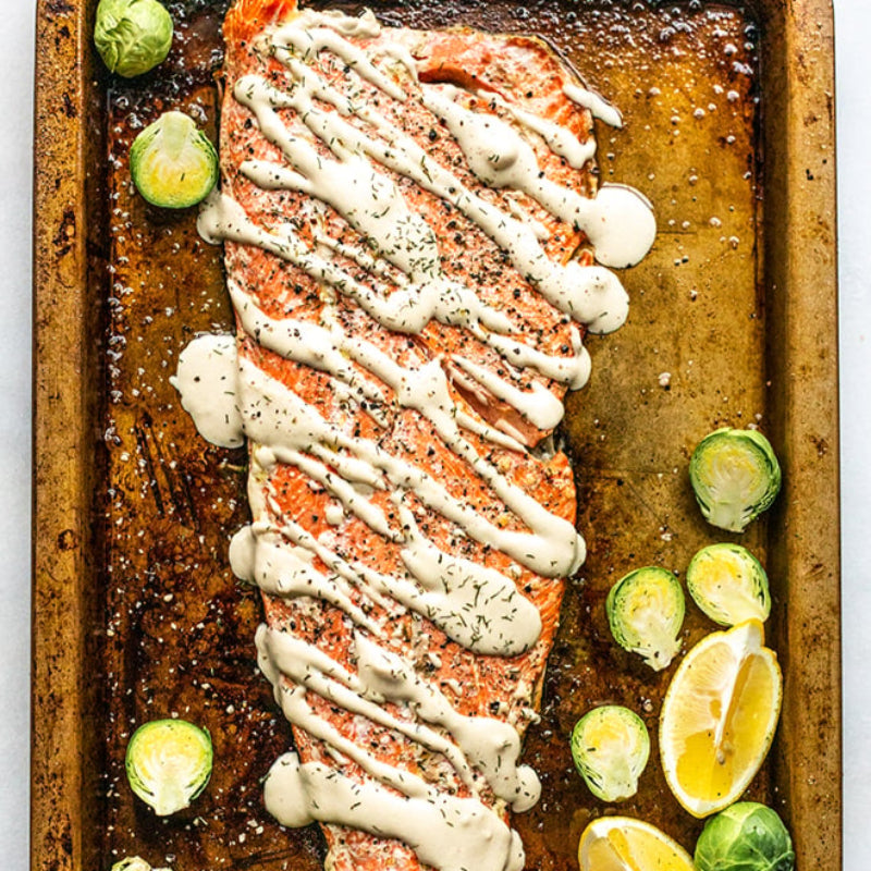 Salmon fillet on a baking tray with drizzle, surrounded by vegetables.