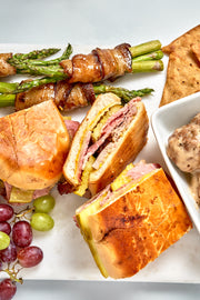 Assorted food items including sandwiches, asparagus, grapes, and bread on a white plate.